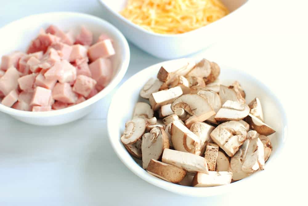 Chopped mushrooms in a bowl next to a bowl of ham