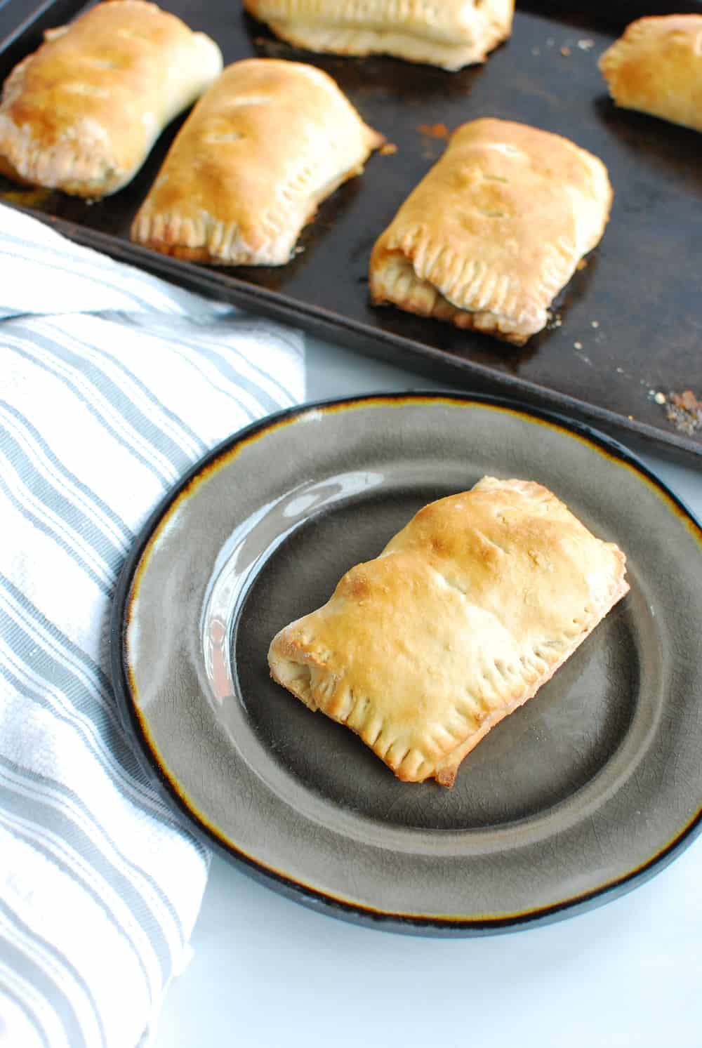 A homemade ham and cheese pocket on a plate next to a tray of them