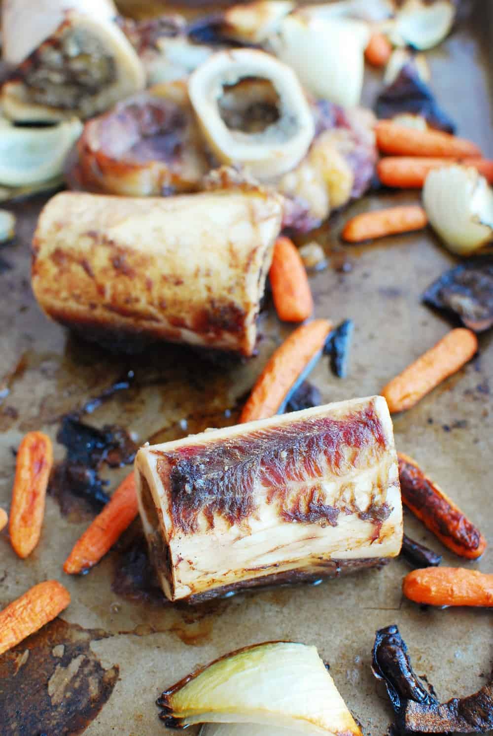 A bunch of beef bones and vegetables roasted on a baking sheet