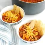 Two bowls of healthy turkey chili topped with cheddar and tortilla chips