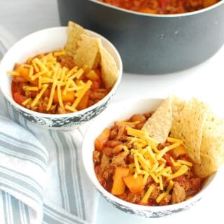 Two bowls of healthy turkey chili topped with cheddar and tortilla chips