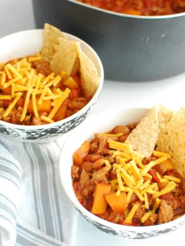 Two bowls of healthy turkey chili topped with cheddar and tortilla chips.