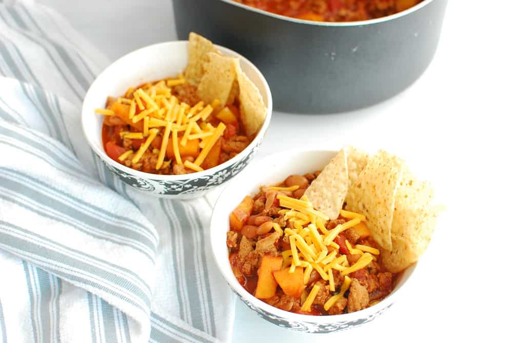 Two bowls of healthy turkey chili topped with cheddar and tortilla chips