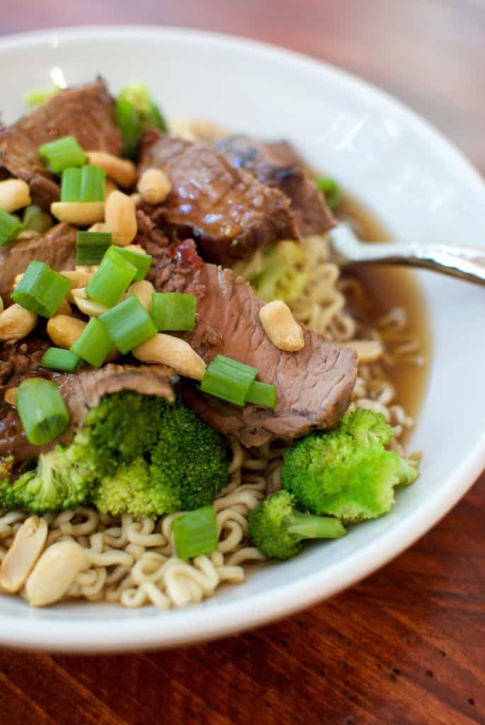 Beef and broccoli ramen in a white bowl topped with peanuts.