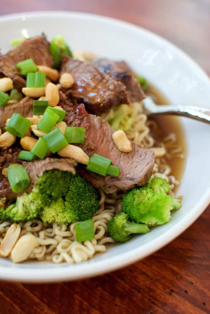 Beef and broccoli ramen in a white bowl topped with peanuts.