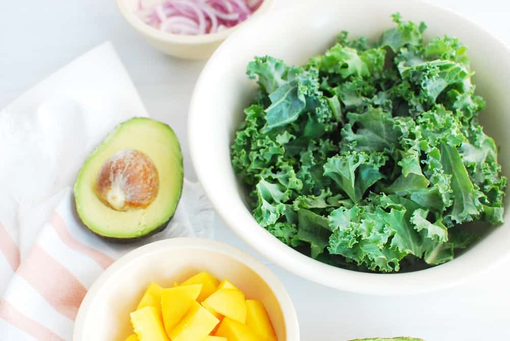 Ingredients to make a healthy salad including kale, mango, avocado and red onion