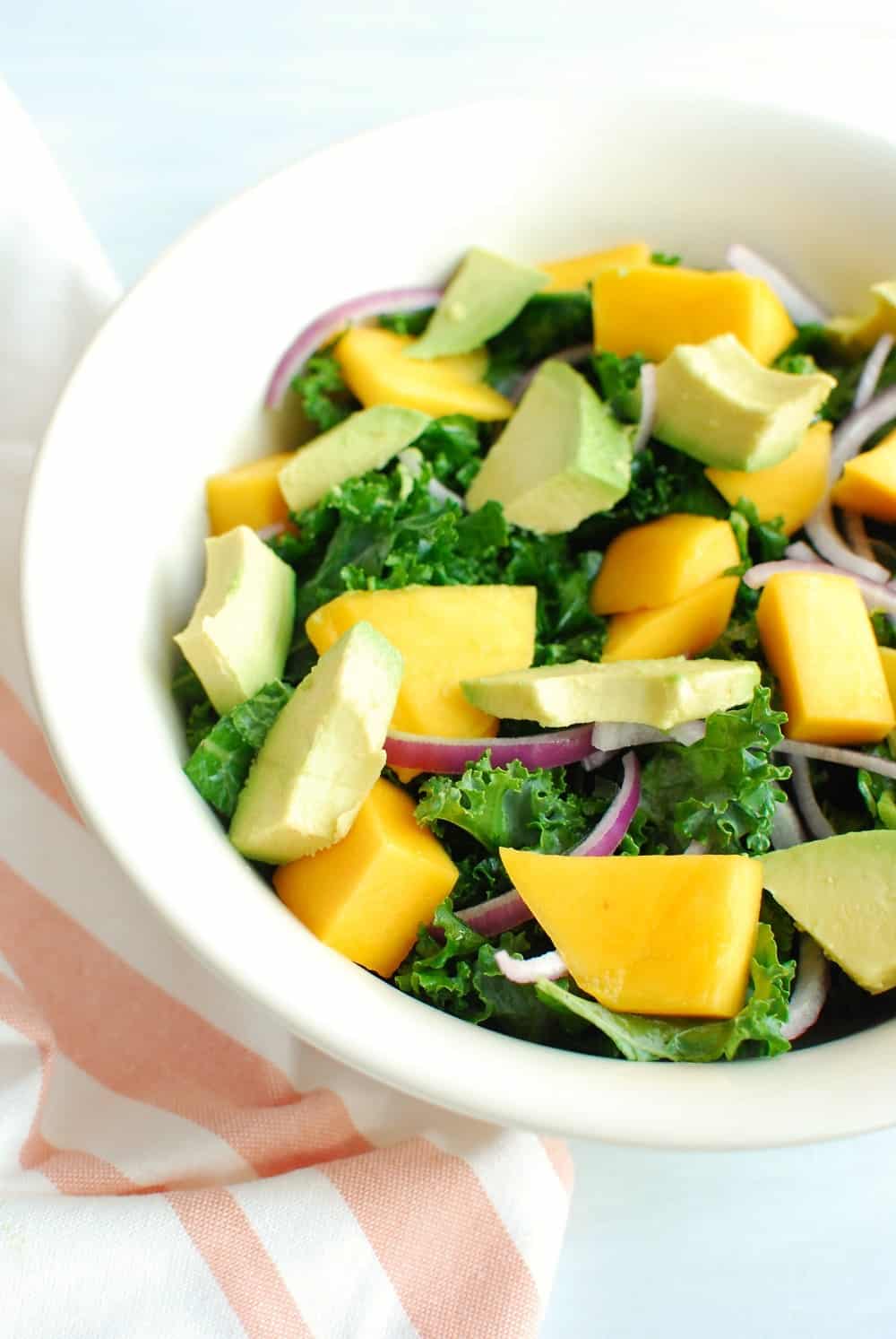 A bowl full of kale salad with mango, avocado, and red onion