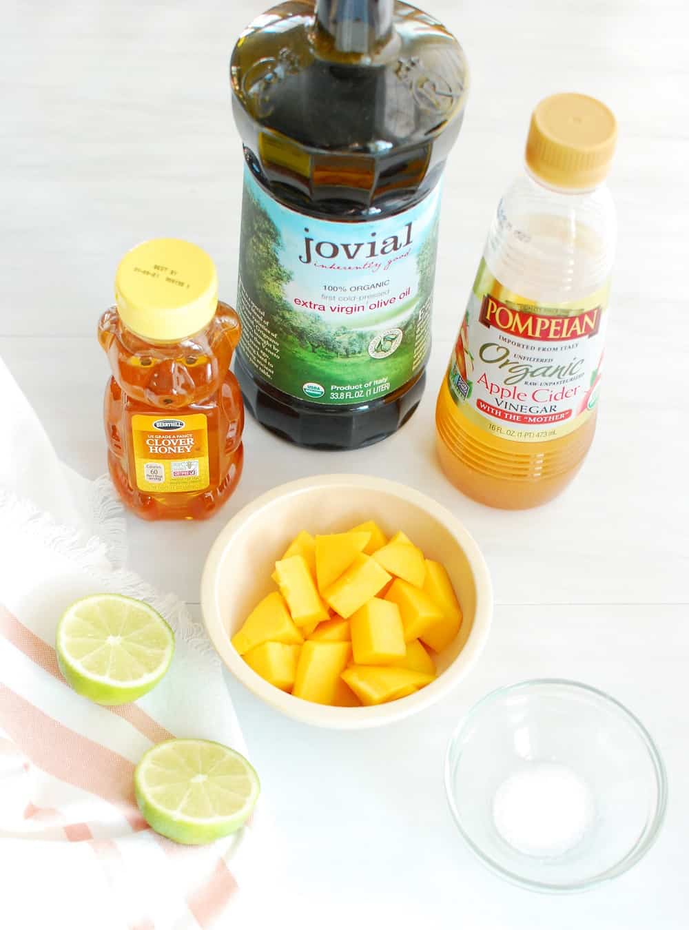 Ingredients to make a homemade salad dressing including mango, lime, honey, vinegar, oil, and salt