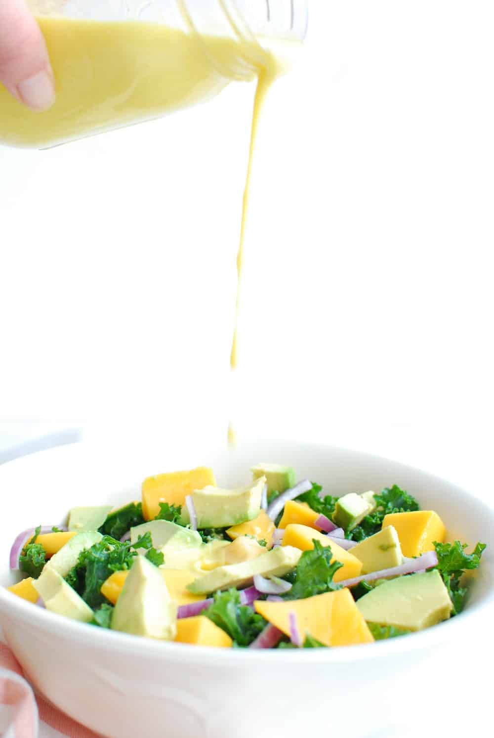 Someone drizzling mango salad dressing into a bowl of salad