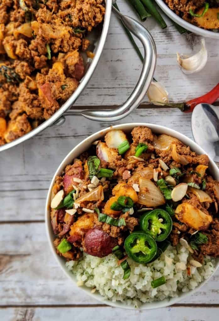 Curry beef bowl on a table beside a skillet.