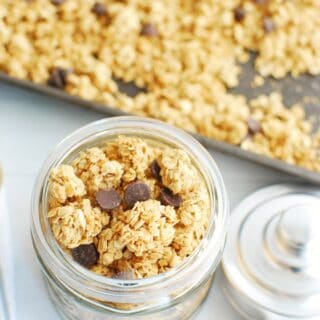 A small jar full of homemade vegan granola next to a large sheet pan of granola