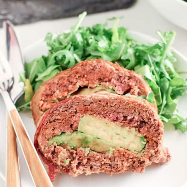 Meatloaf on a white plate beside a salad with utensils.