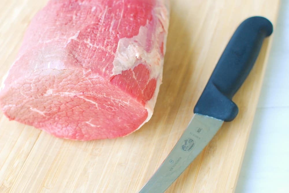 An eye of round roast on a cutting board next to a knife