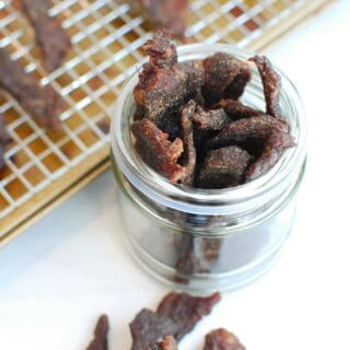 Homemade gluten free beef jerky in a small jar next to a baking sheet