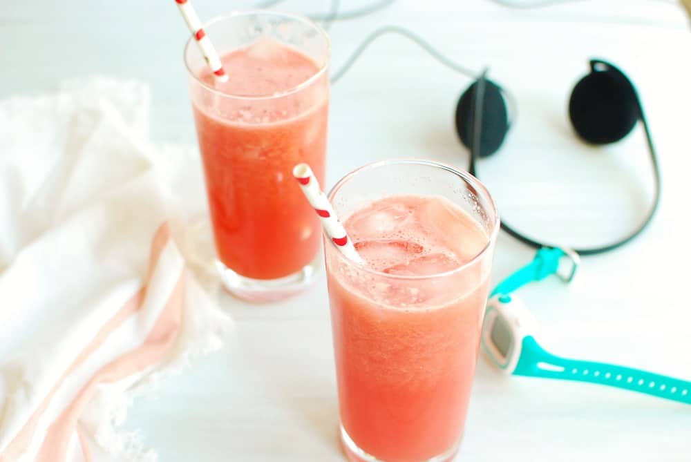 Homemade sports drink in two glasses next to a watch and headphones