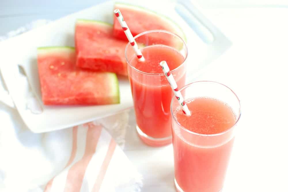Two glasses of homemade sports drink next to a plate of sliced watermelon