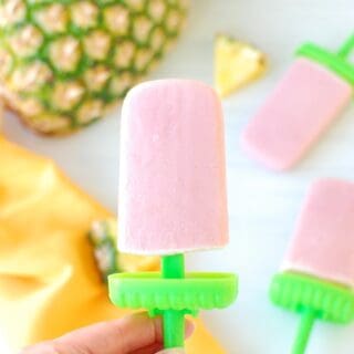 A woman's hand holding a cherry pineapple popsicle