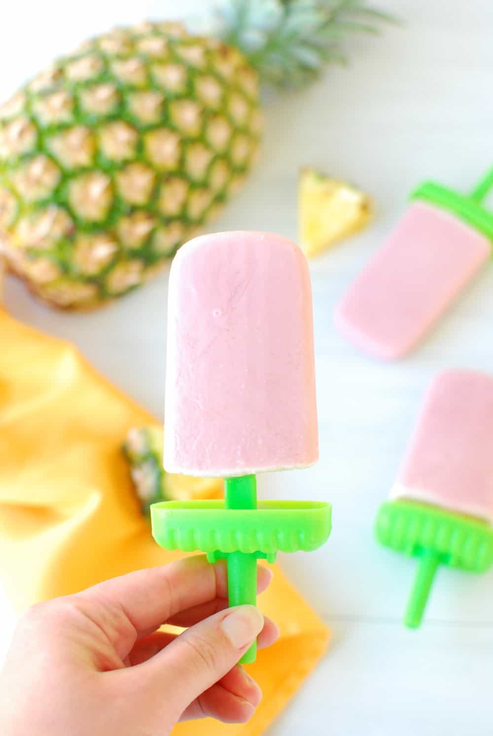 A woman's hand holding a cherry pineapple popsicle