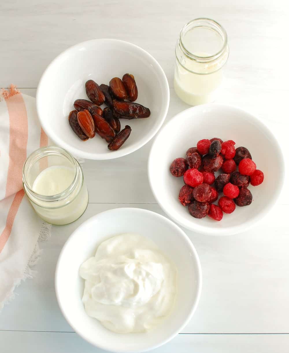 A bowl of cherries, greek yogurt, and dates, next to glasses of milk and cream