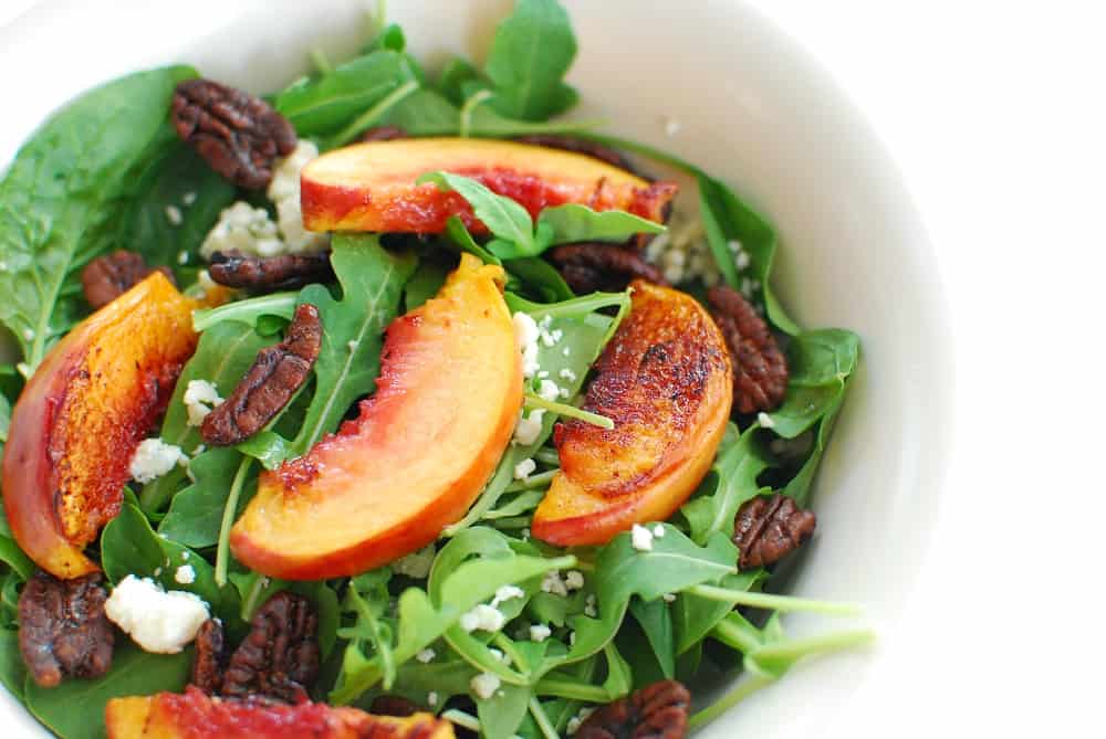 Close up of a spinach arugula salad with peaches, pecans, and blue cheese