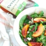 A bowl of arugula spinach salad next to a package of honey roasted pecans