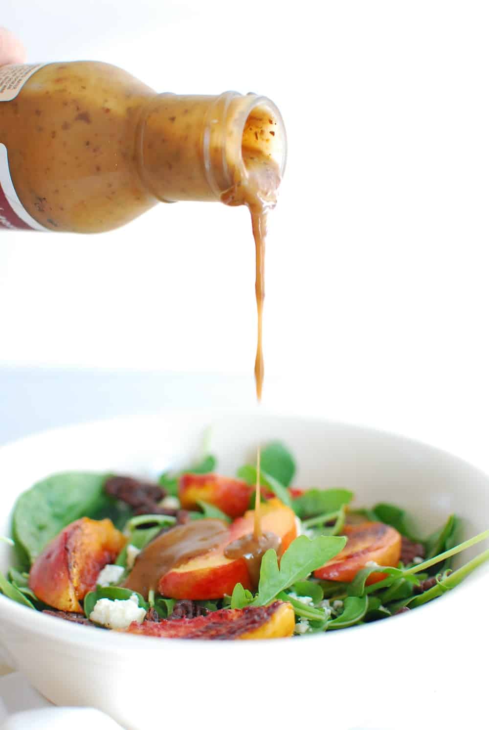 Balsamic dressing being drizzled on top of a spinach arugula salad