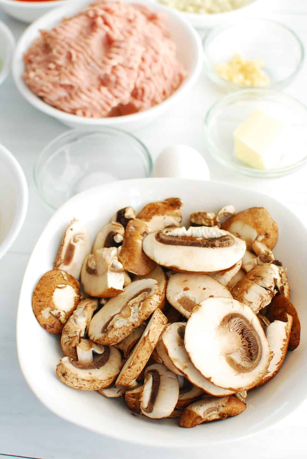 Baby bella mushrooms in a white bowl next to other ingredients