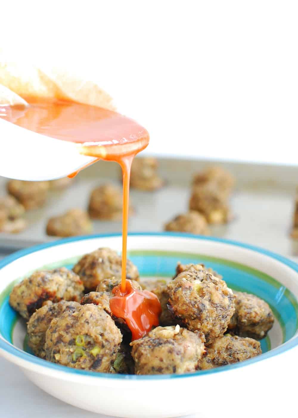 Pouring buffalo sauce over turkey meatballs