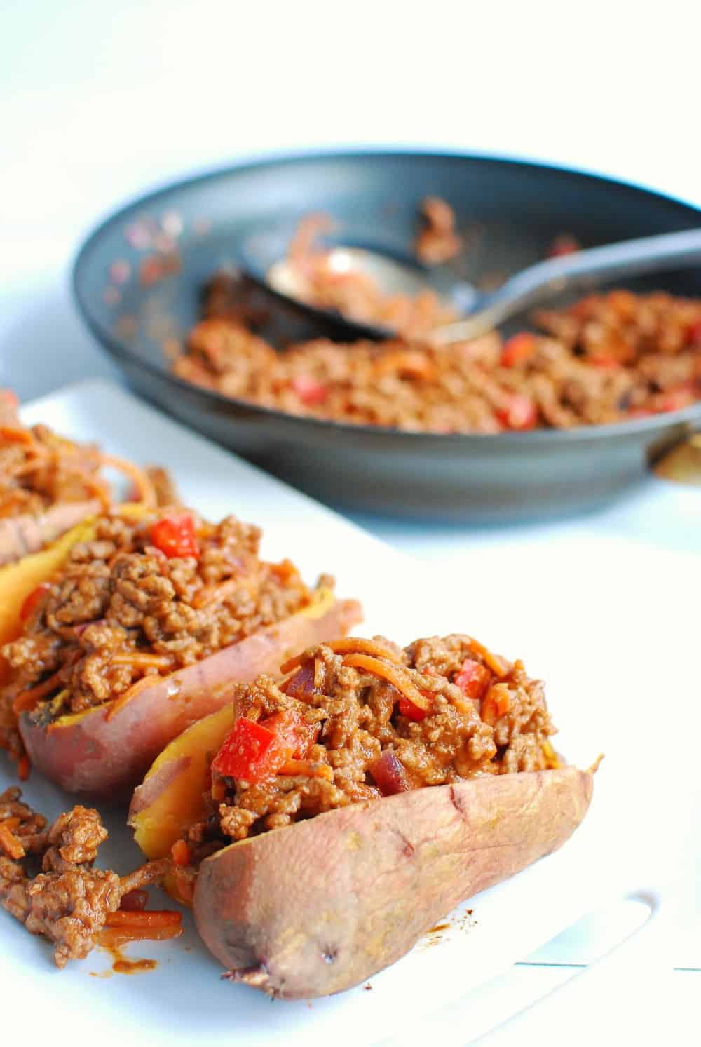 ground beef stuffed sweet potatoes on a white plate next to a pan of bbq beef