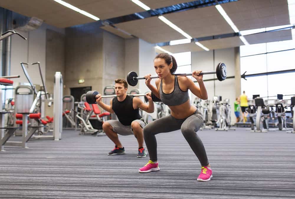 a young man and woman doing squats at a gym