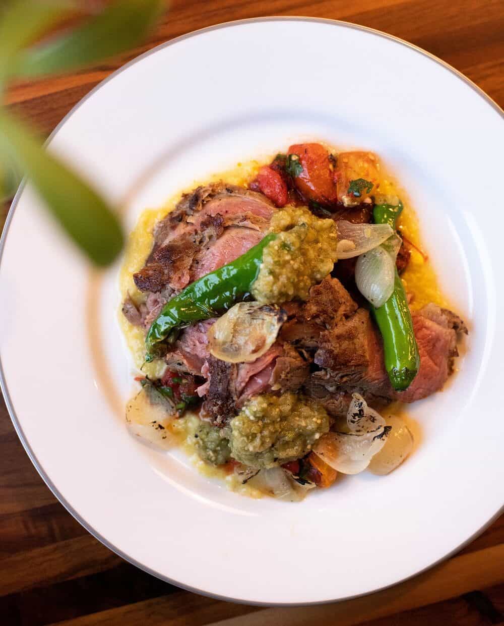 Tri tip steak served over creamed corn on a white plate