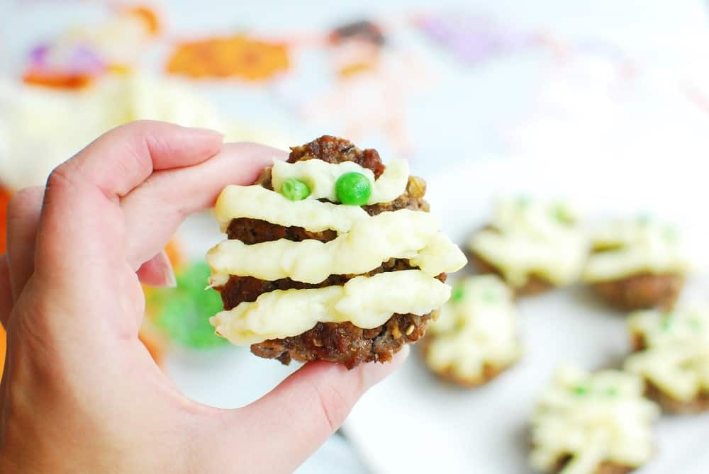 a woman's hand holding mini halloween meatloaves in a mummy theme