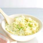 A bowl of Greek yogurt mashed potatoes with a wooden serving spoon.