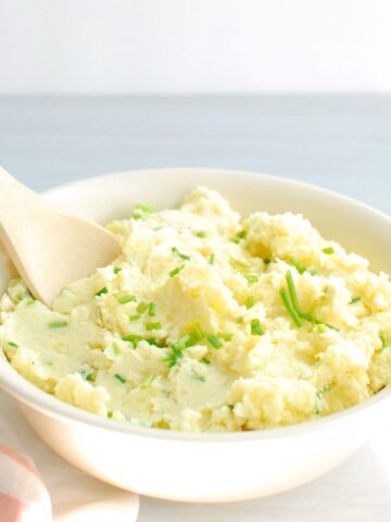 A bowl of Greek yogurt mashed potatoes with a wooden serving spoon.