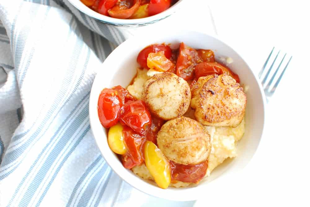 A bowl with scallops and grits next to a striped napkin