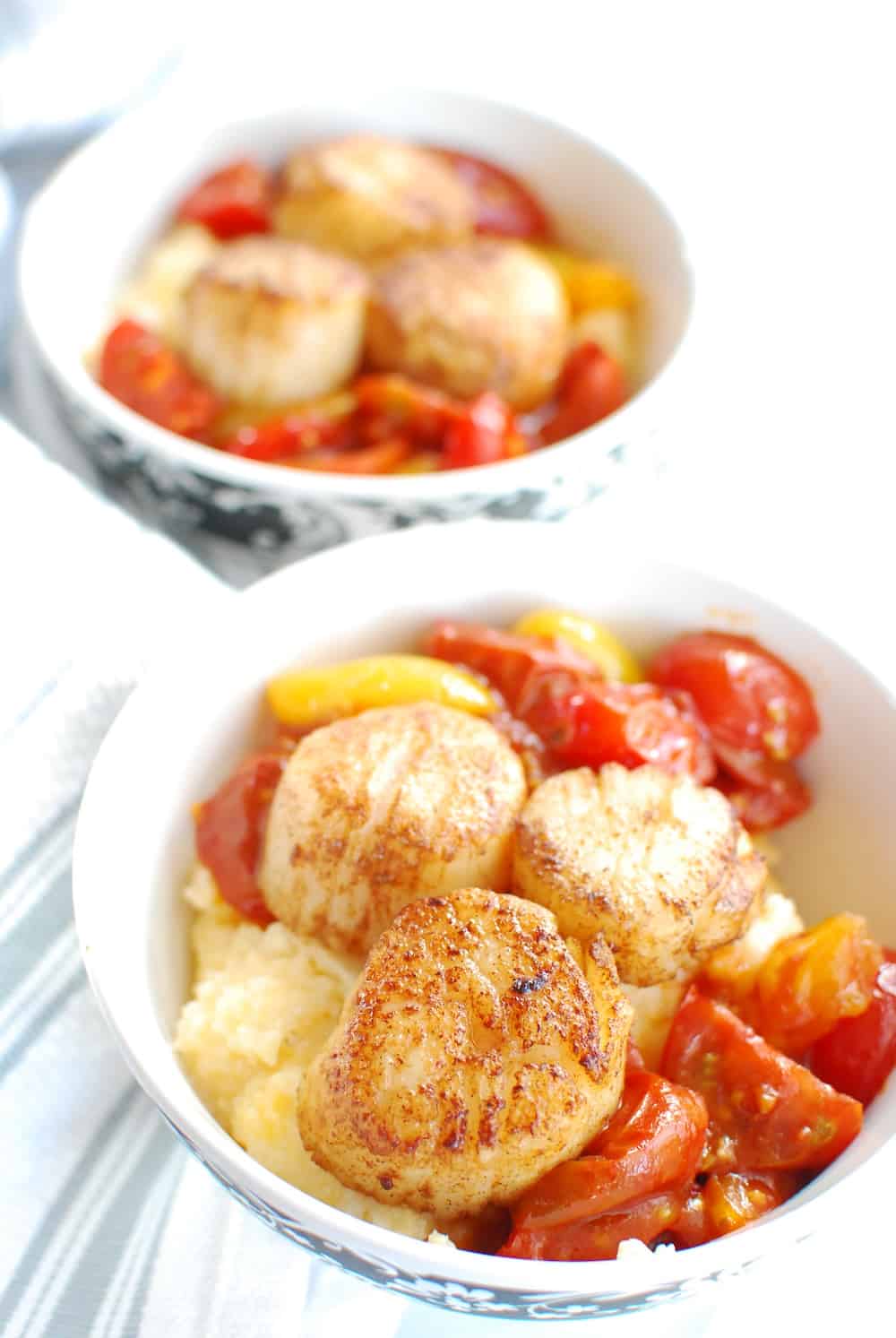 A bowl full of scallops and grits along with balsamic cherry tomatoes