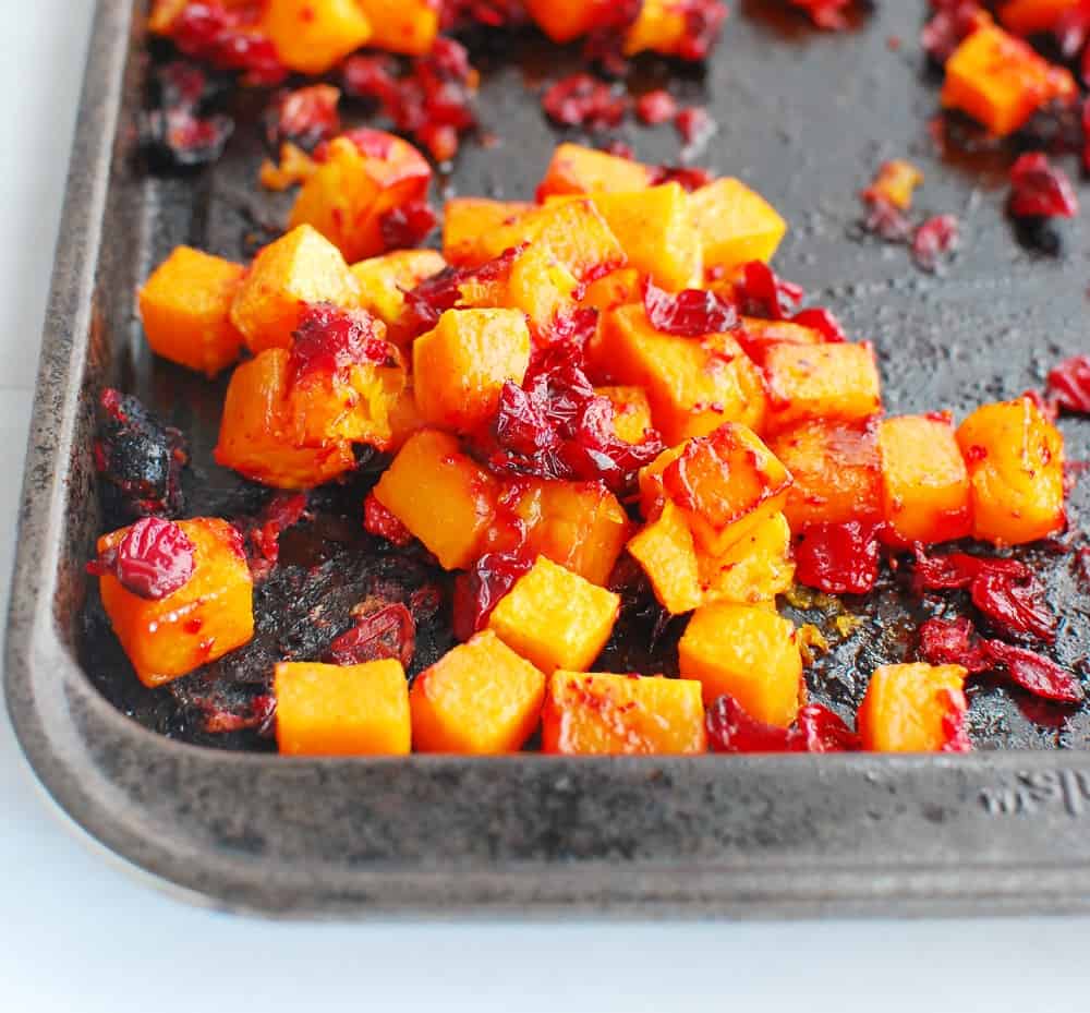 butternut squash and cranberries on a baking sheet after being cooked in the oven