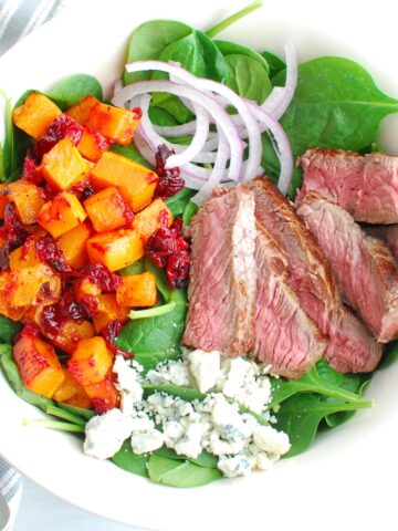 A steak salad with butternut squash, cranberries, blue cheese, and red onion.