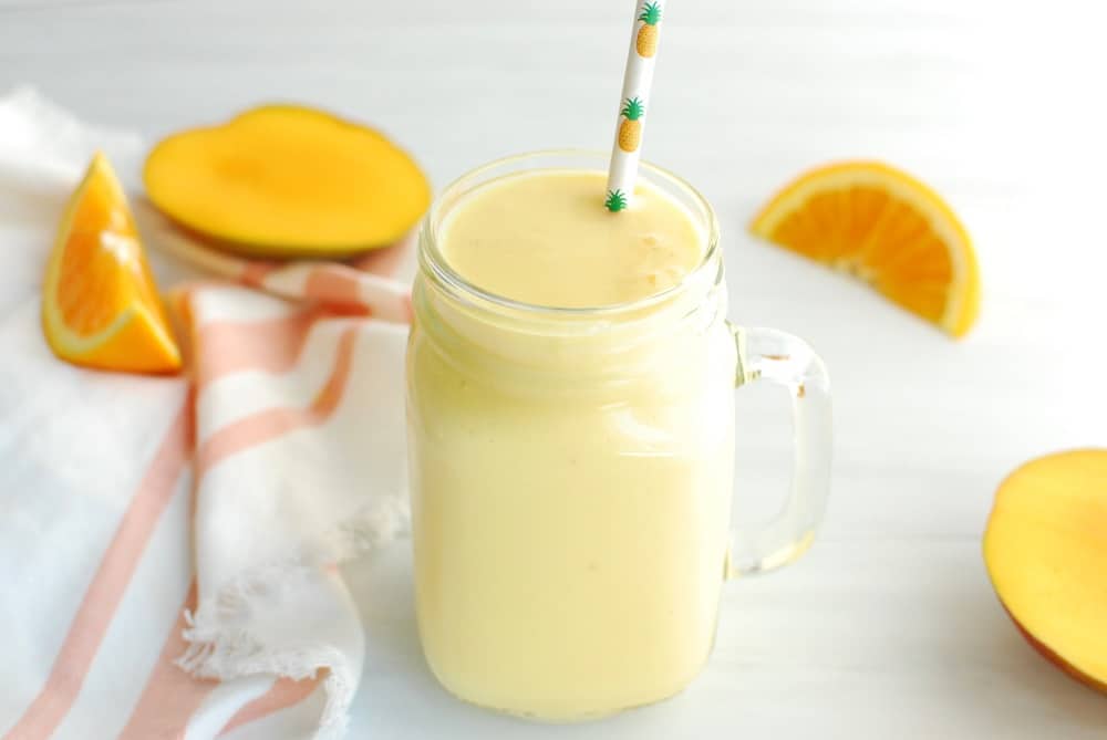 A mango pineapple post run smoothie in a mason jar next to fresh cut fruit