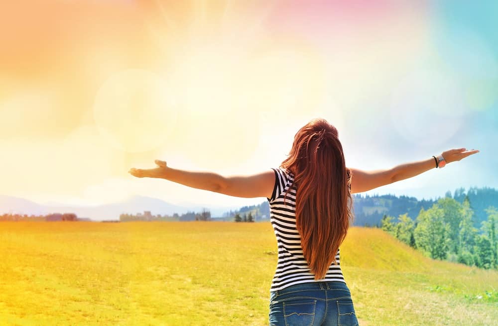 a woman feeling inspired by the one word challenge, standing outside with her arms open towards the sky