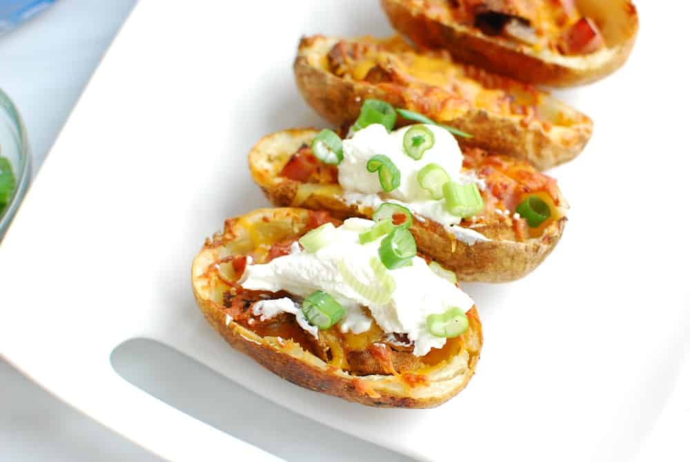 Air fryer potato skins on a platter, some of which are topped with sour cream and green onions