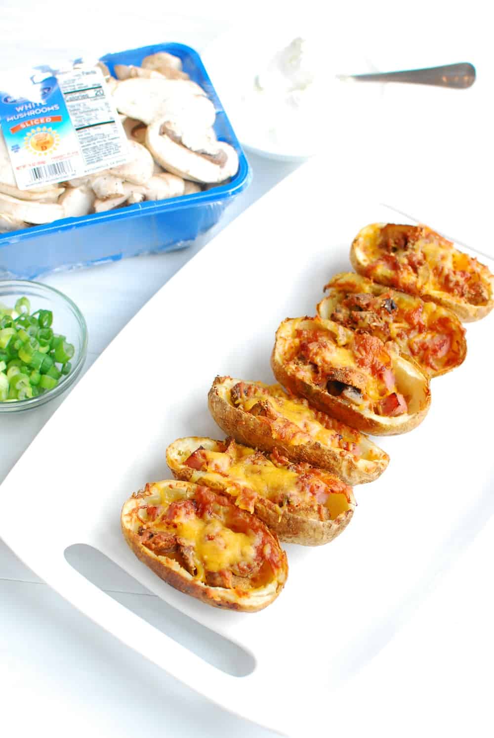 a white platter of air fried potato skins next to a package of mushrooms and a bowl of green onions