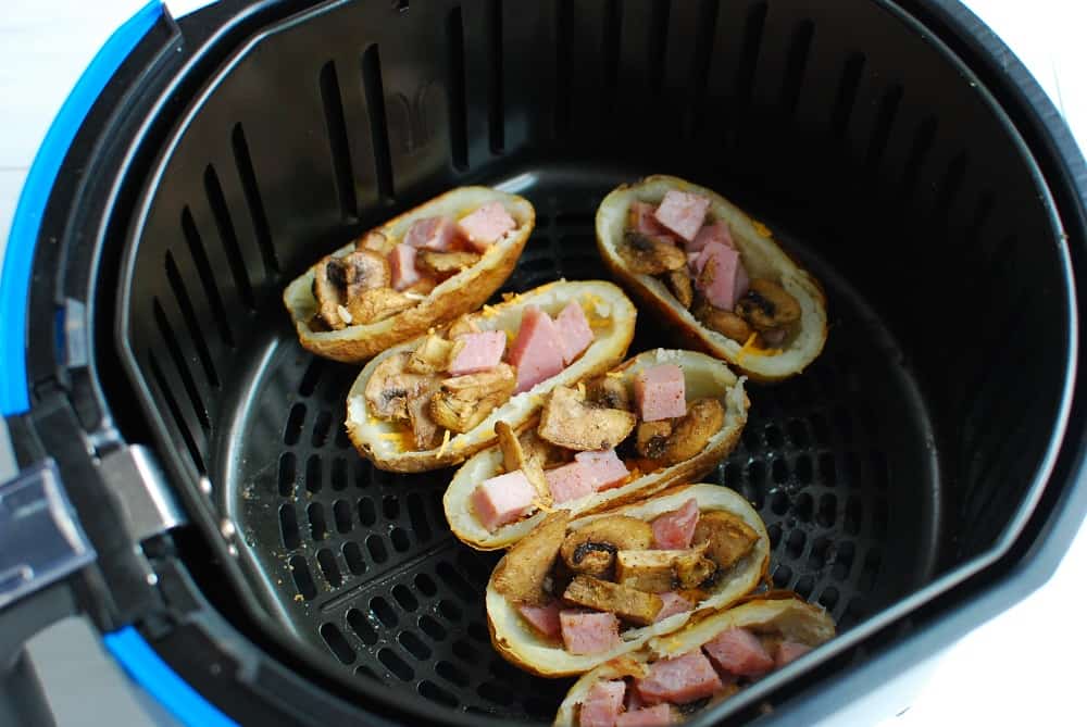 Potato skins stuffed with cheese, mushrooms, and ham, placed in the air fryer prior to cooking