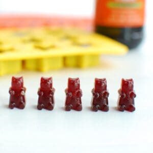 5 elderberry gummy bears on a table with a gummy bear mold in the background.