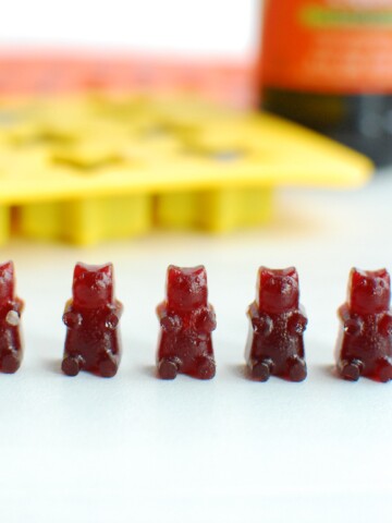 5 elderberry gummy bears on a table with a gummy bear mold in the background.