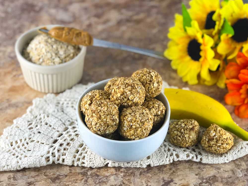 A bowl full of peanut butter banana energy bites next to a banana and a small bowl of oats.