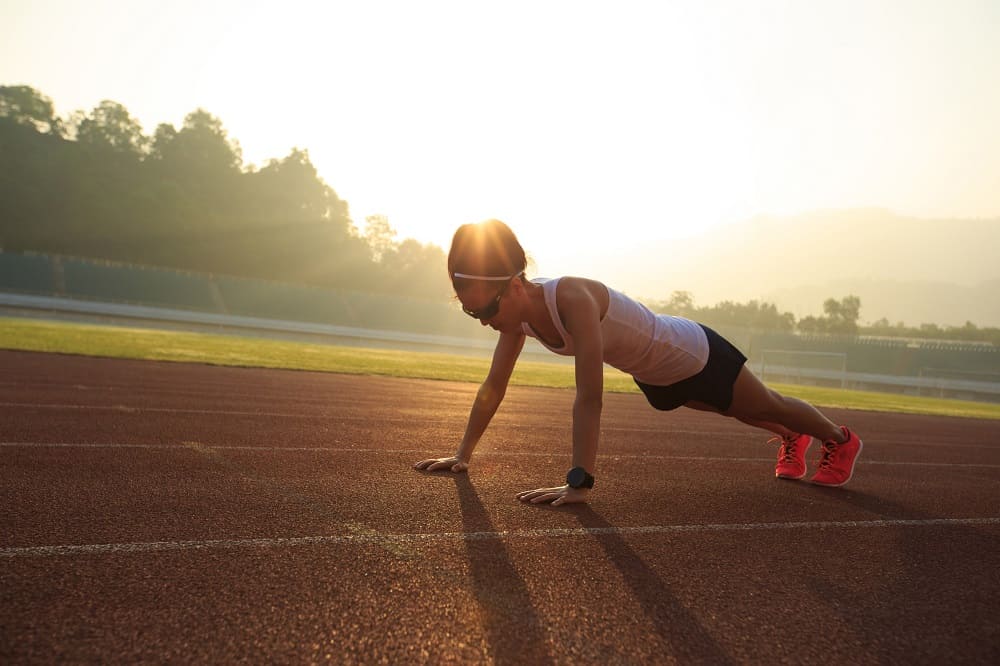 a woman doing push ups outside on a track