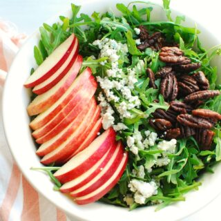A bowl filled with arugula, apples, blue cheese, and pecans