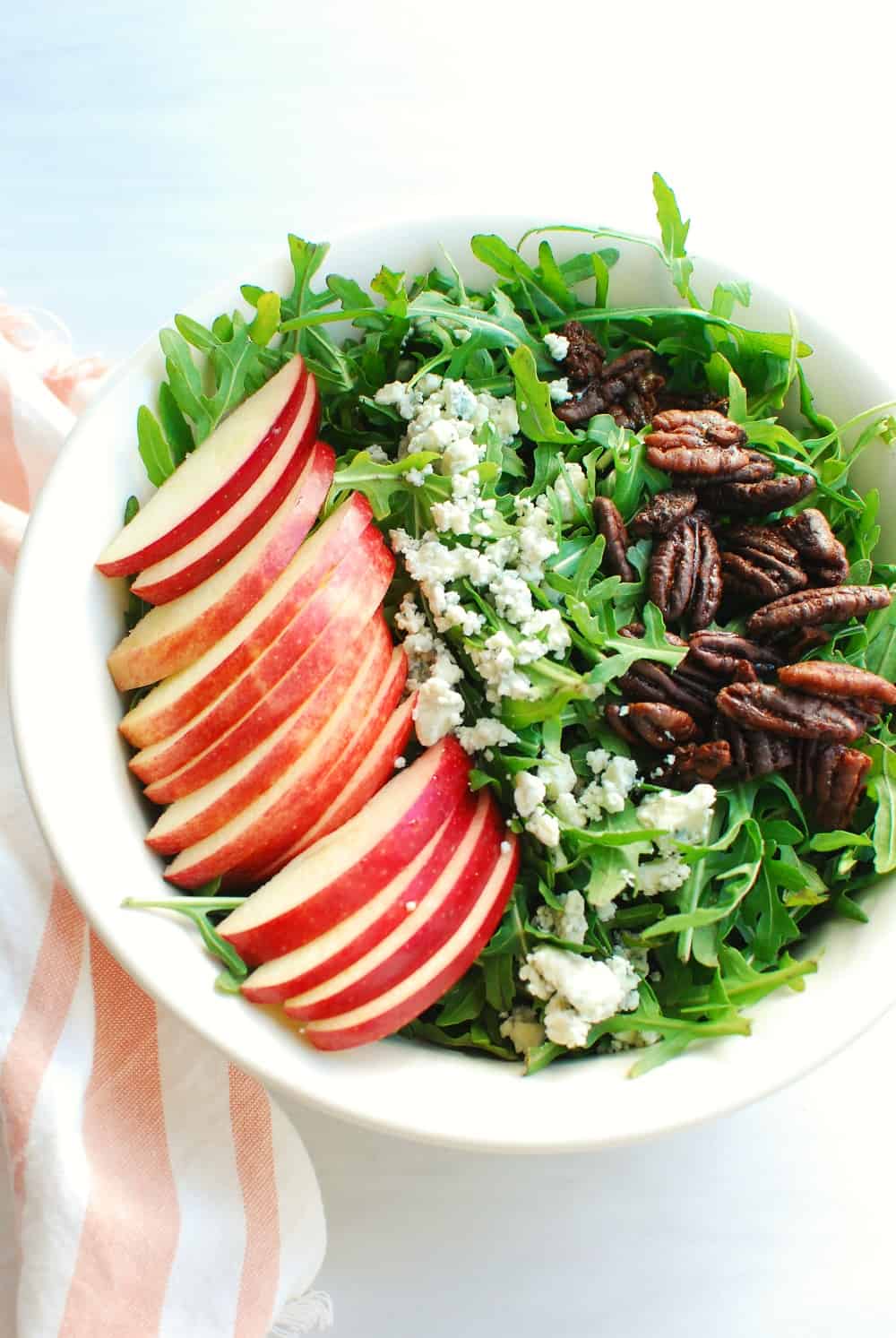 A bowl filled with arugula, apples, blue cheese, and pecans