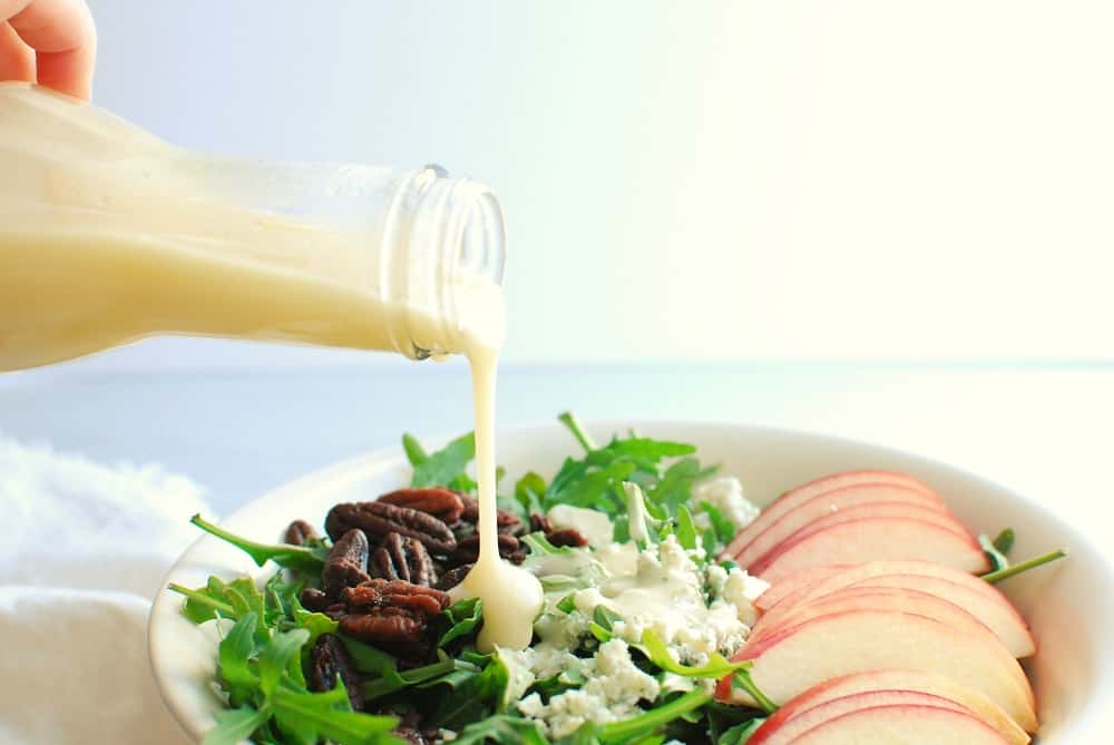 A woman pouring dressing on a salad